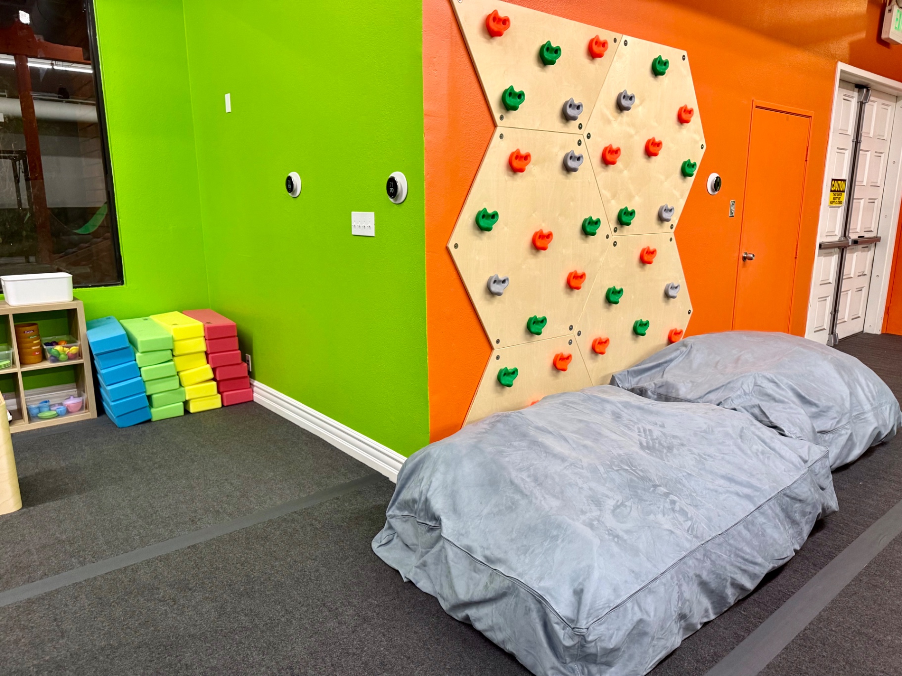 Hexagonal climbing wall and crash pads against bright green and orange walls at Arcadia