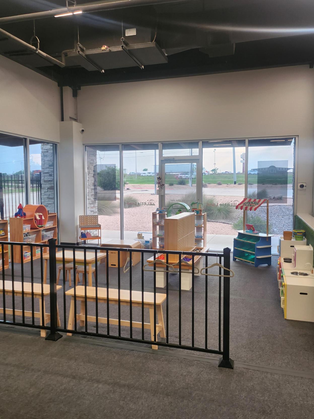 Light-filled play area with large front windows, wooden play shelves, and a pretend market stand