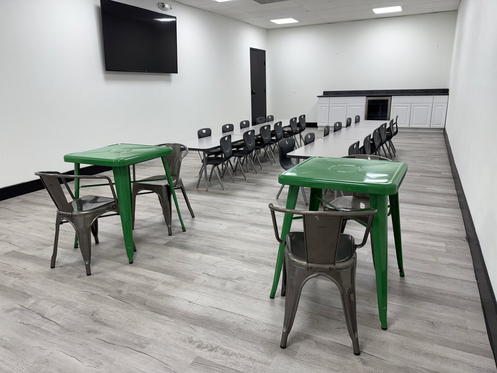 Party and event room at Little Land Cedar Park with green kid tables, long banquet table, and a mounted TV