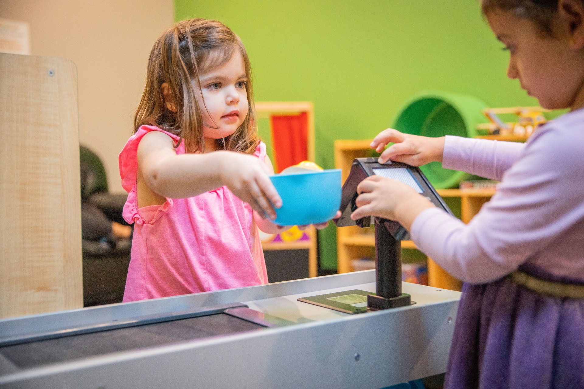 Two children pour and explore at a colorful sensory table in the play gym