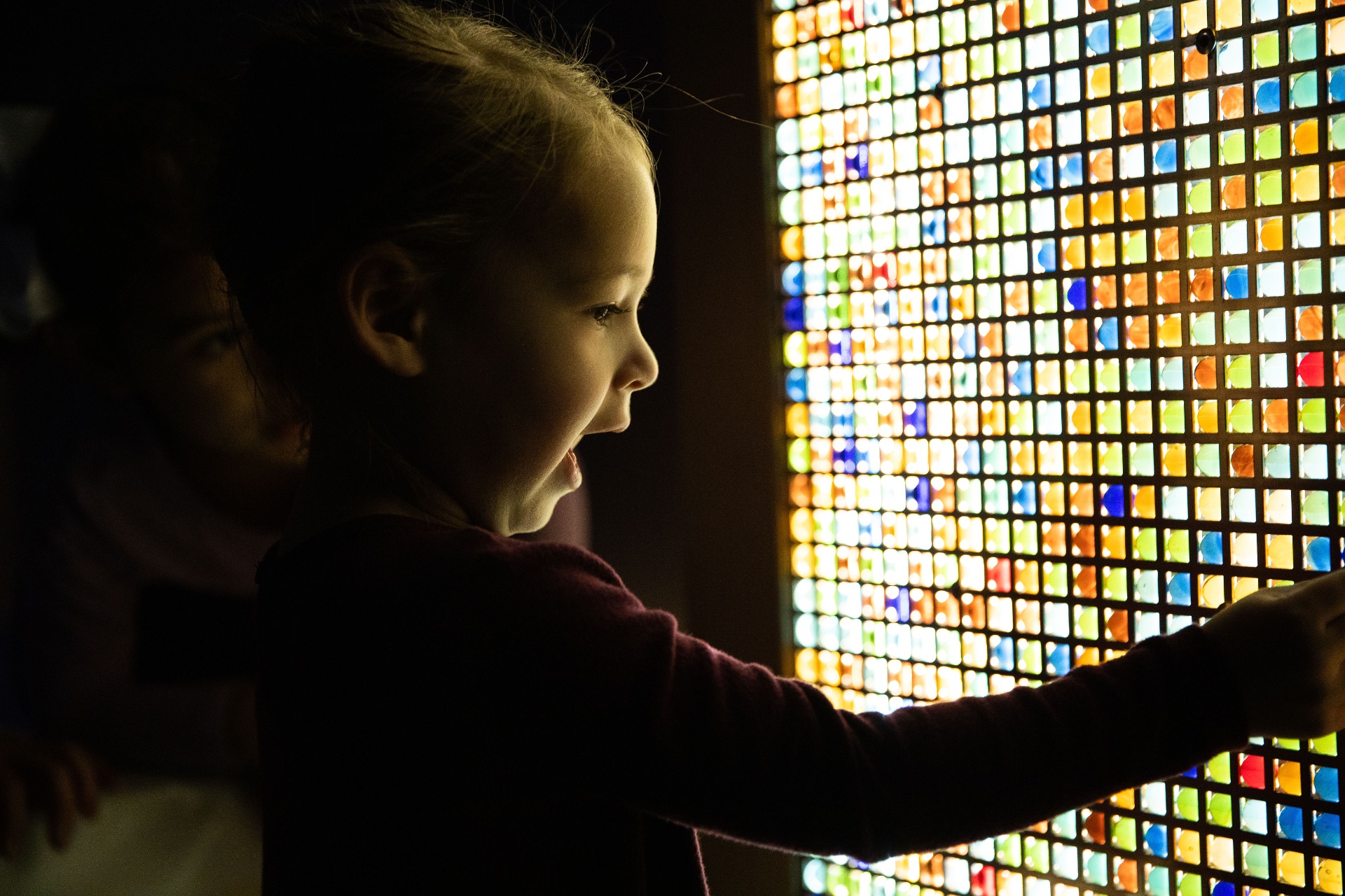 Child wide-eyed in front of a glowing stained-glass light wall