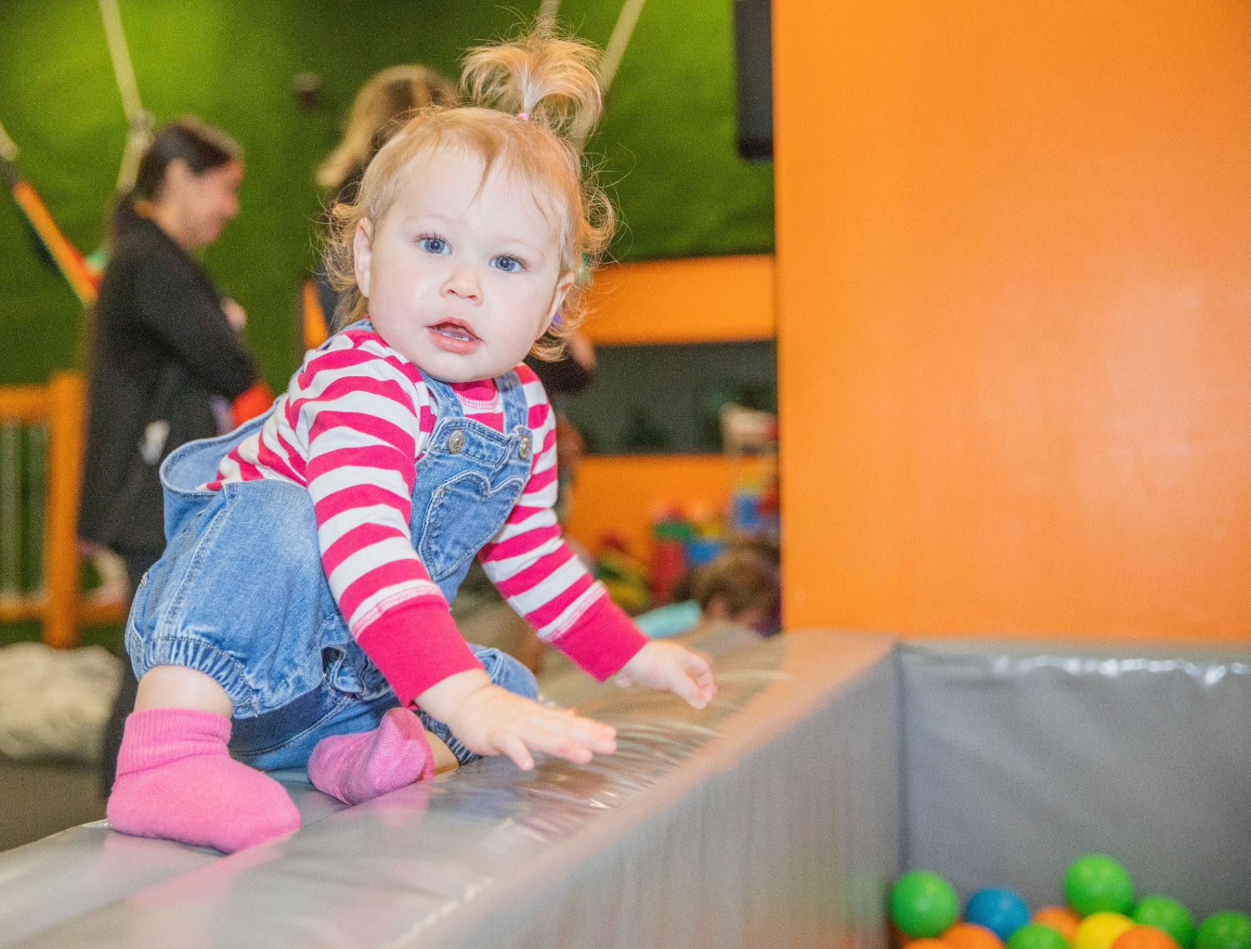Toddler in overalls climbing into a ball pit