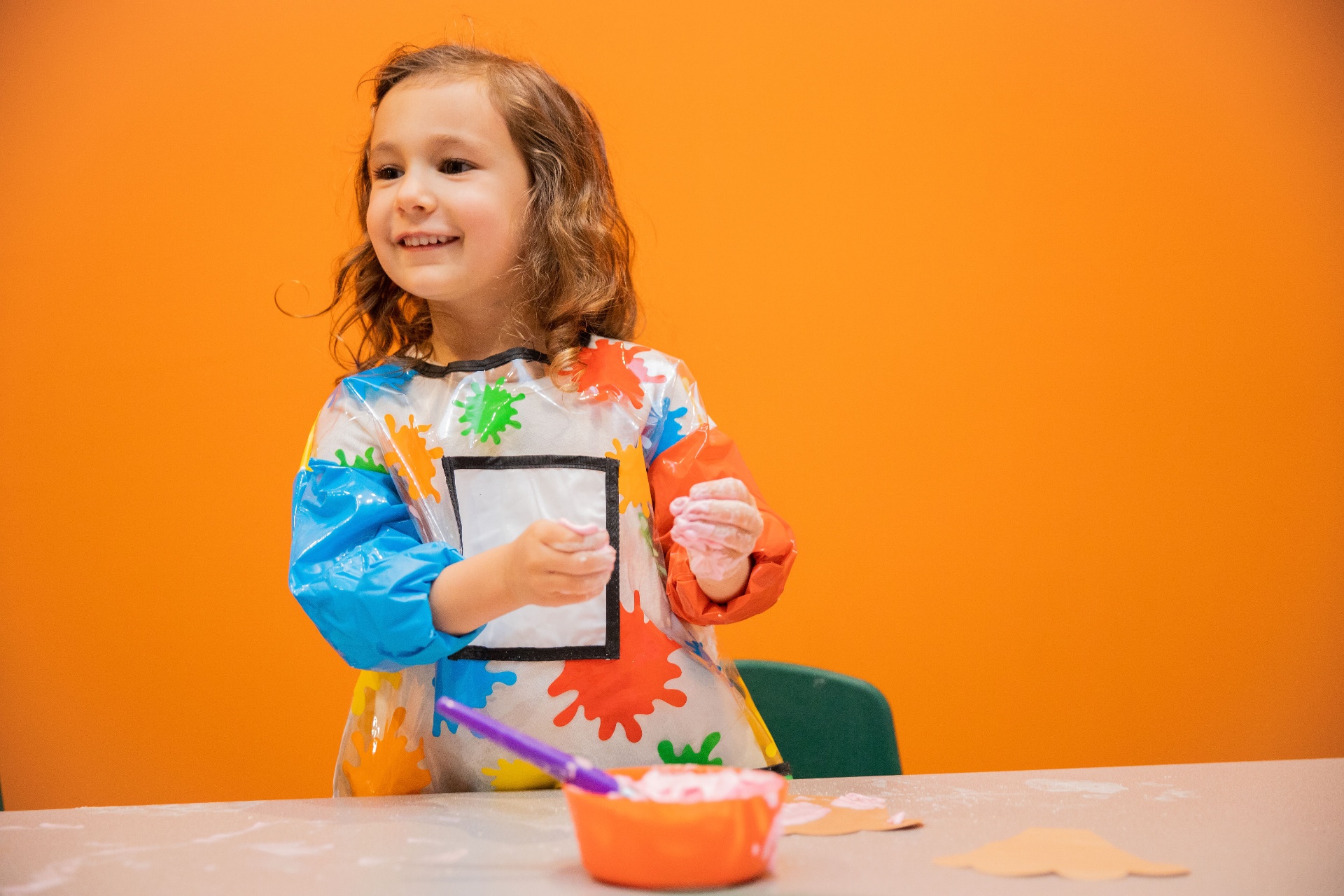 A smiling child in a paint smock at the art table