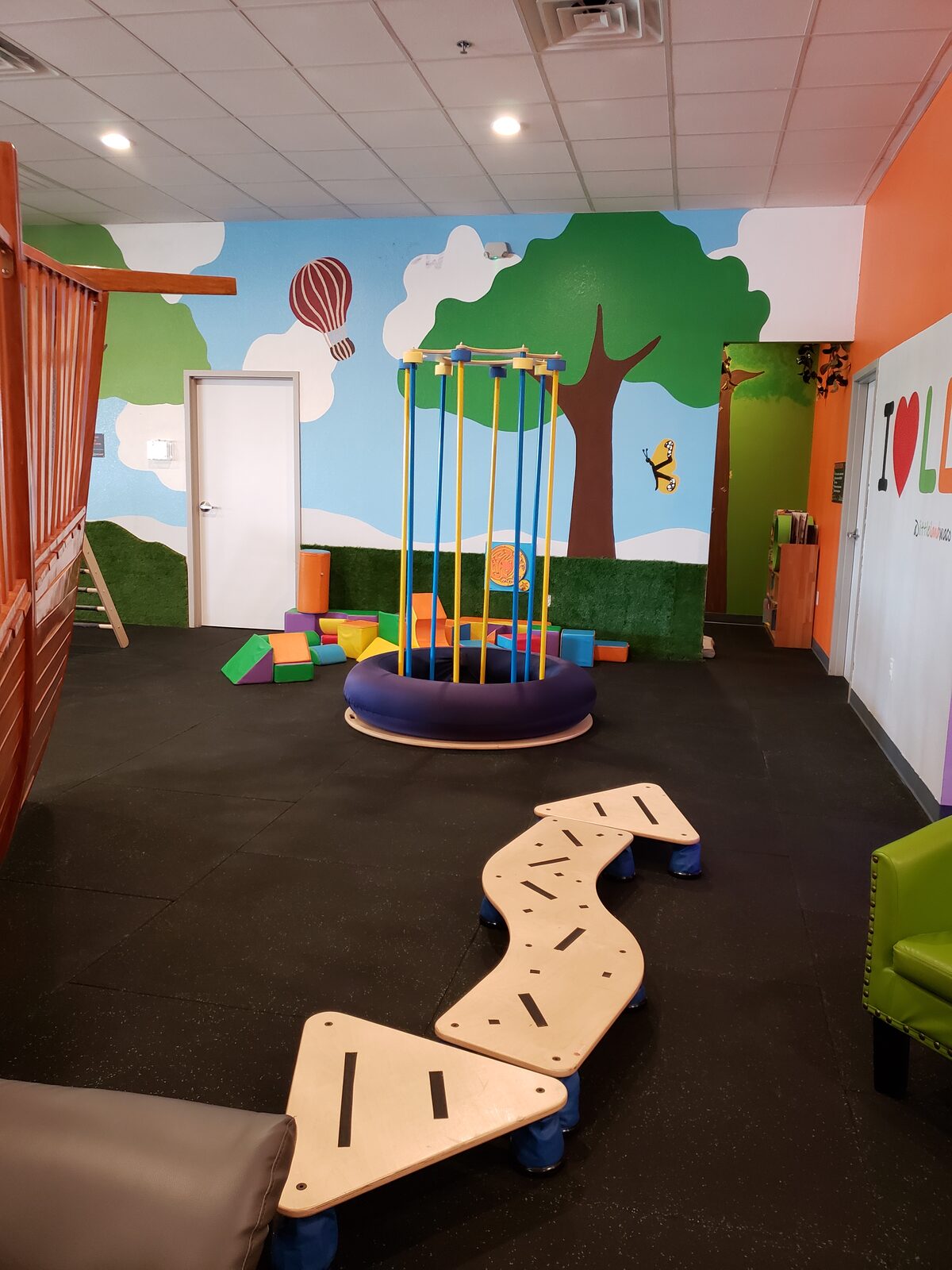Carousel swing and balance path in front of a hand-painted tree mural at Little Land Waco